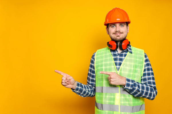 Construction safety worker wearing helmet and high-visibility vest pointing direction against yellow background.