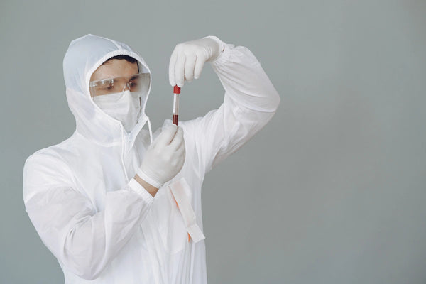 Healthcare professional in protective equipment handling a blood sample tube for laboratory safety and bloodborne pathogens prevention training.