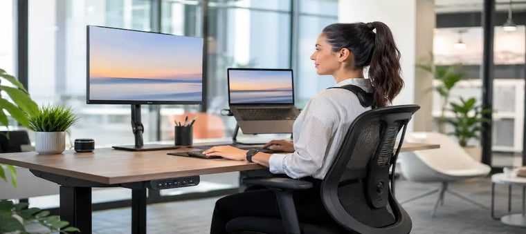 Woman working at an ergonomic desk with dual screens.