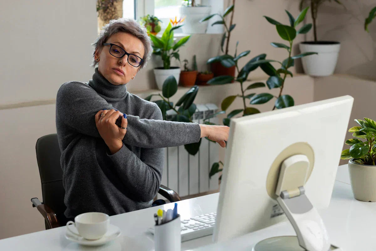 Woman stretching her shoulder while seated at a computer desk.