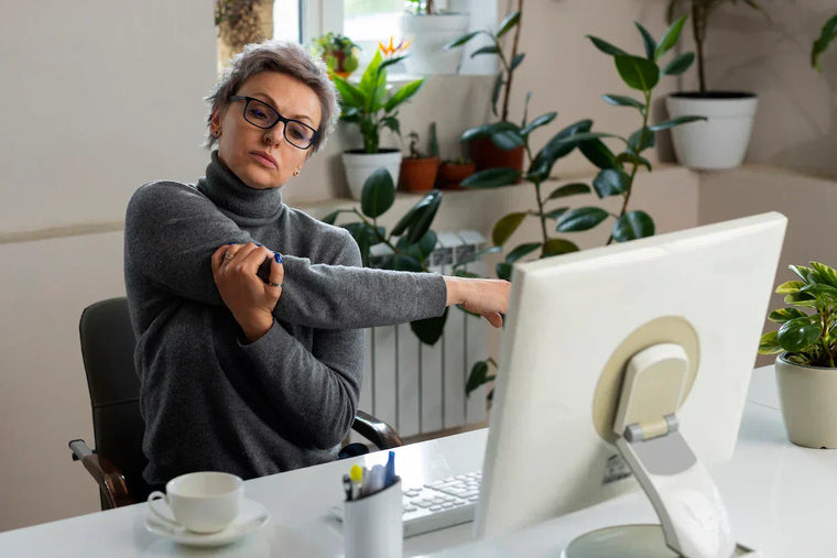 Woman stretching her shoulder while seated at a computer desk.